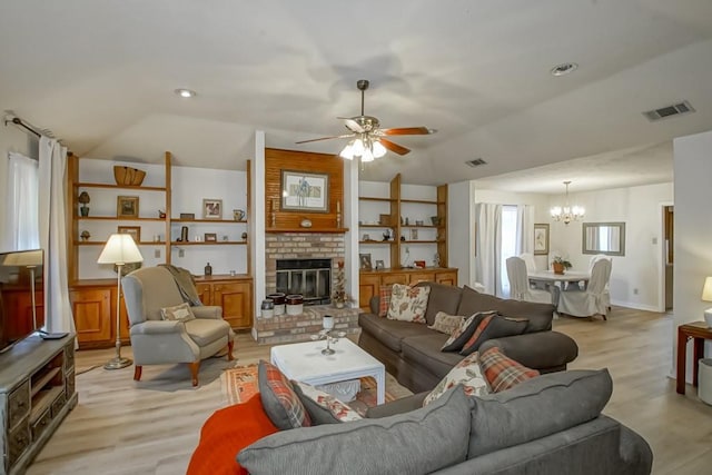 living room with ceiling fan with notable chandelier, lofted ceiling, a fireplace, and light hardwood / wood-style floors