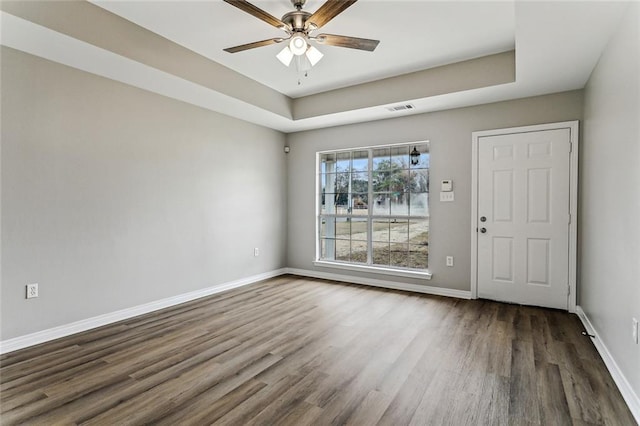 unfurnished room featuring dark wood-type flooring, ceiling fan, and a tray ceiling