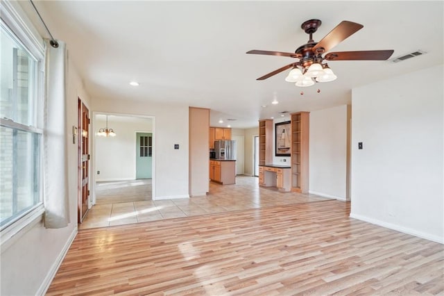 unfurnished living room with ceiling fan with notable chandelier and light hardwood / wood-style floors