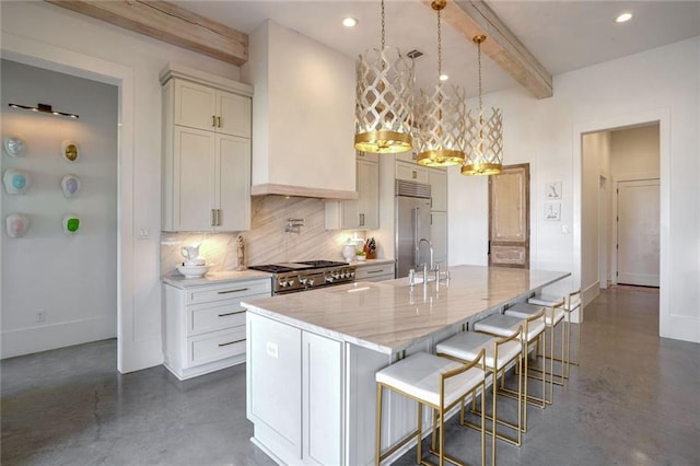 kitchen with hanging light fixtures, stove, stainless steel built in fridge, light stone countertops, and a center island with sink