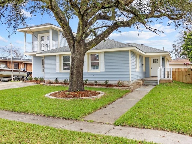 view of front of home featuring a front lawn, roof with shingles, fence, and a balcony