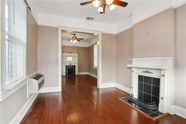 unfurnished living room with a tiled fireplace, dark wood-type flooring, a wall mounted AC, and ceiling fan