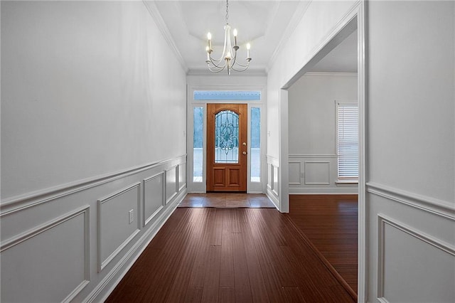 foyer entrance with ornamental molding, a decorative wall, dark wood-style flooring, and an inviting chandelier