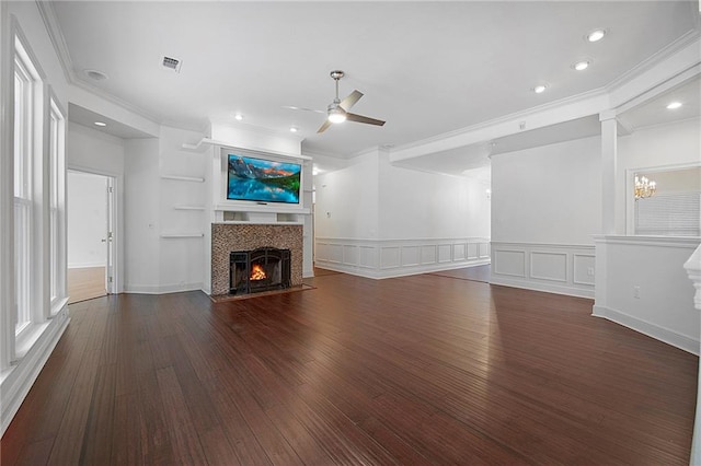 unfurnished living room with a tile fireplace, a decorative wall, dark wood-style flooring, visible vents, and a ceiling fan