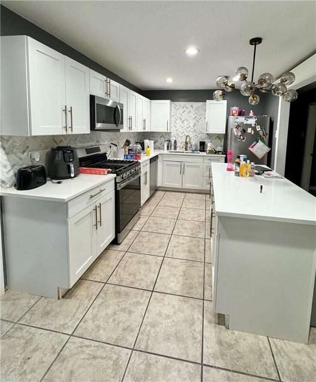 kitchen with light tile patterned floors, backsplash, stainless steel appliances, white cabinets, and decorative light fixtures