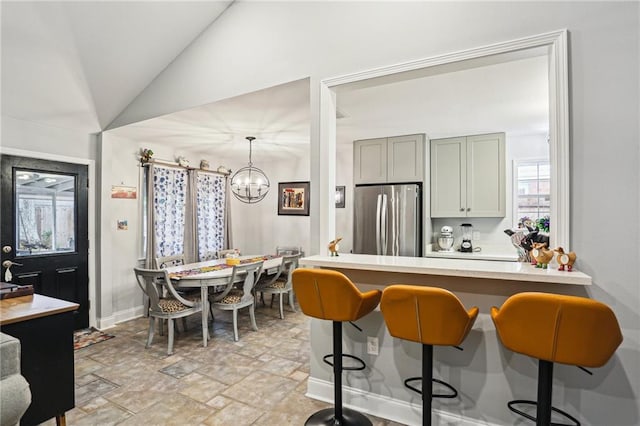 kitchen featuring gray cabinets, vaulted ceiling, a breakfast bar, pendant lighting, and stainless steel refrigerator