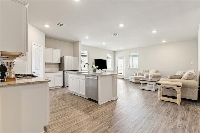 kitchen featuring dishwasher, white cabinets, fridge, light hardwood / wood-style floors, and a center island with sink