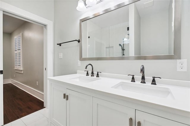 full bath featuring double vanity, a shower with door, baseboards, and a sink