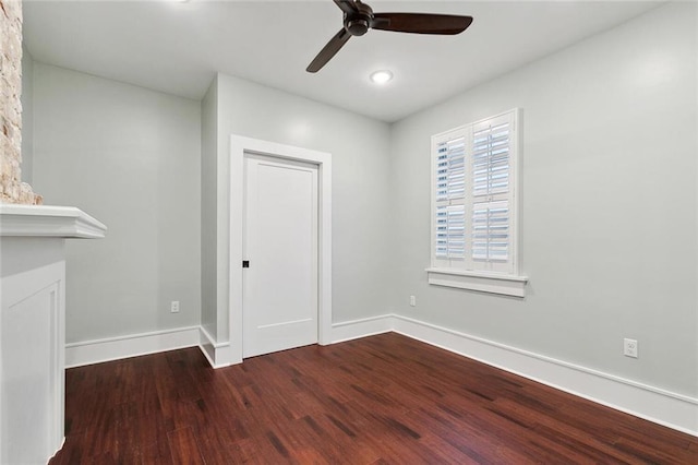 empty room featuring a large fireplace, ceiling fan, baseboards, and wood finished floors