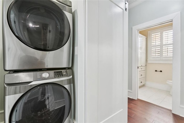 clothes washing area with a barn door, laundry area, wood finished floors, baseboards, and stacked washing maching and dryer