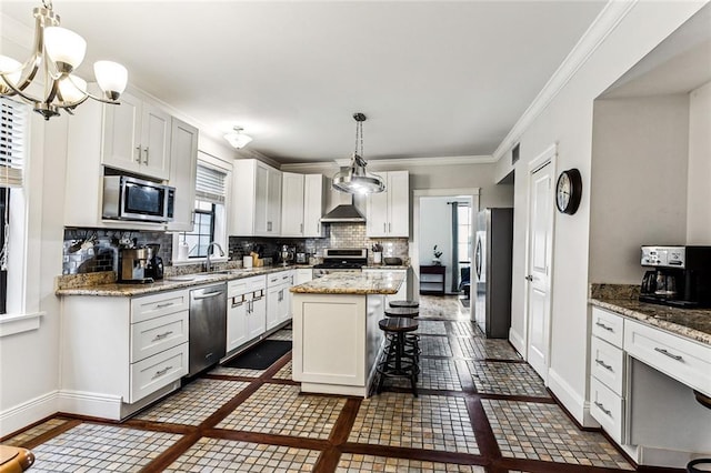 kitchen featuring wall chimney range hood, appliances with stainless steel finishes, a center island, white cabinets, and decorative light fixtures