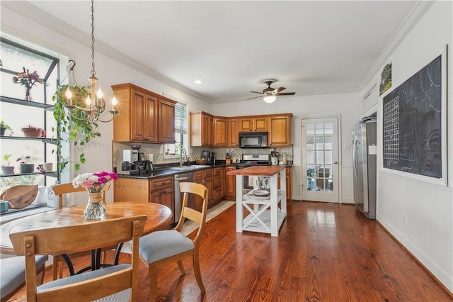 kitchen with dark wood-type flooring, ornamental molding, pendant lighting, stainless steel appliances, and decorative backsplash