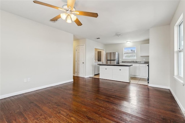 unfurnished living room featuring hardwood / wood-style flooring, washer / dryer, and ceiling fan