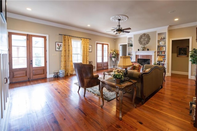 living room featuring hardwood / wood-style flooring, a tiled fireplace, ceiling fan, crown molding, and french doors