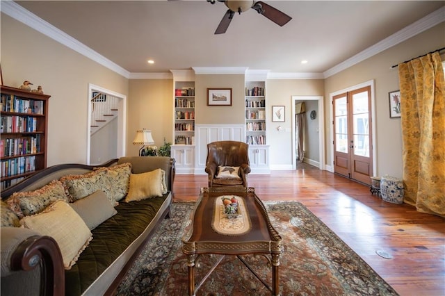 living room featuring hardwood / wood-style floors, built in features, ceiling fan, crown molding, and french doors