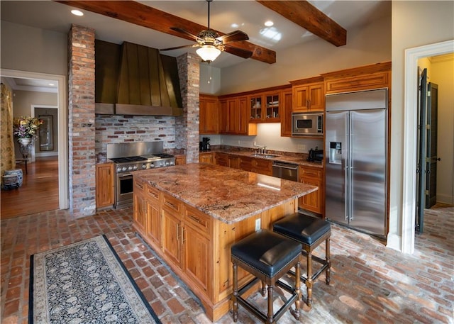 kitchen with light stone counters, built in appliances, a center island, a kitchen breakfast bar, and wall chimney range hood