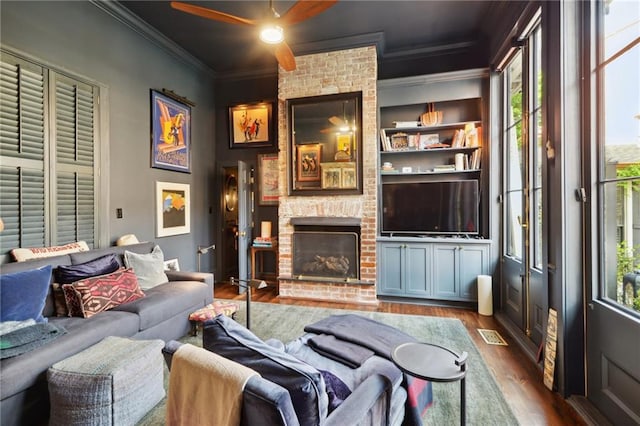 living room with dark wood-type flooring, a fireplace, ornamental molding, and built in shelves