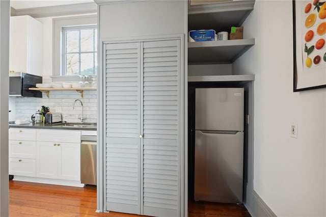 kitchen featuring appliances with stainless steel finishes, white cabinetry, sink, backsplash, and light hardwood / wood-style flooring