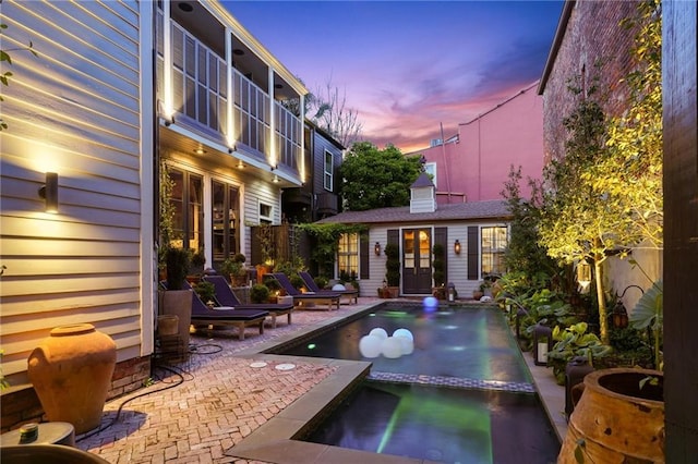 pool at dusk featuring an in ground hot tub, an outdoor structure, and a patio area