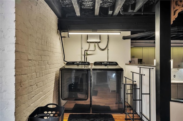 washroom featuring brick wall, separate washer and dryer, and wood-type flooring