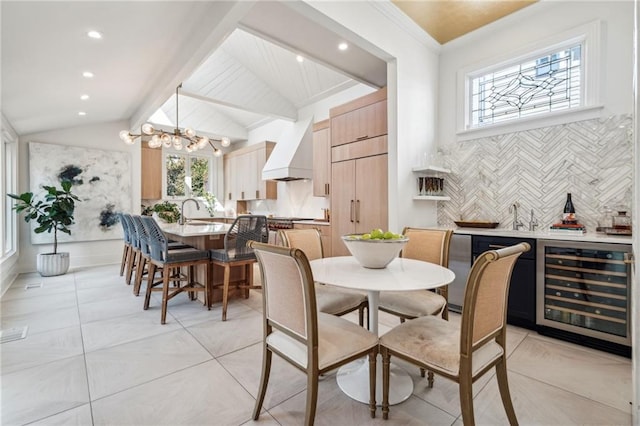 tiled dining space with lofted ceiling, sink, an inviting chandelier, ornamental molding, and beverage cooler