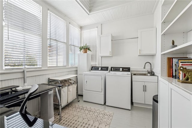 clothes washing area with sink, washing machine and dryer, and cabinets