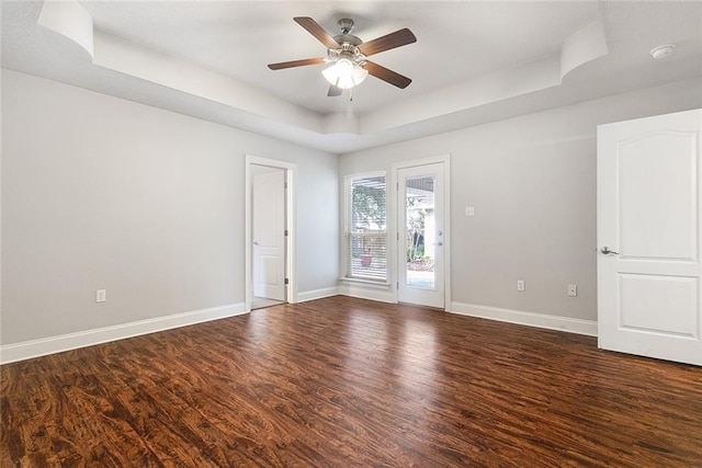 unfurnished room with a tray ceiling, dark wood-type flooring, and ceiling fan