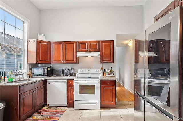 kitchen featuring a towering ceiling, stainless steel appliances, sink, and light tile patterned floors