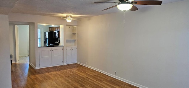 interior space featuring ceiling fan, a textured ceiling, baseboards, and wood finished floors