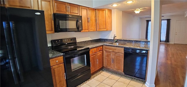 kitchen with black appliances, dark stone countertops, a sink, and brown cabinets