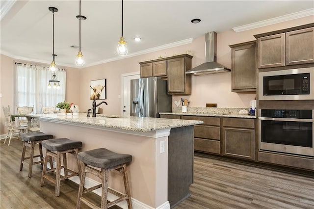 kitchen featuring wall chimney range hood, sink, hanging light fixtures, black appliances, and a center island with sink