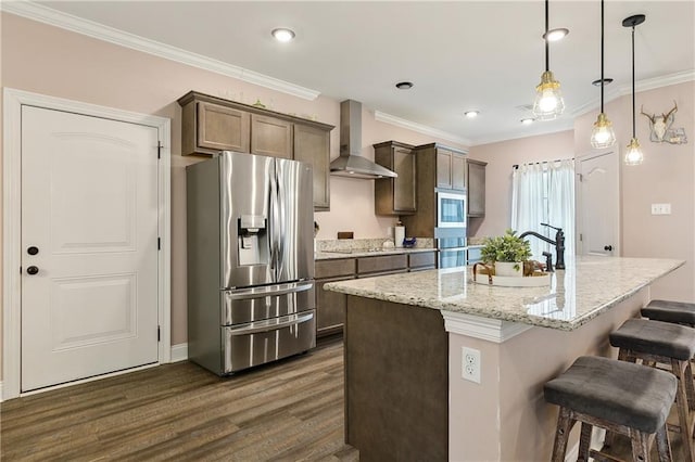 kitchen with sink, wall chimney range hood, appliances with stainless steel finishes, an island with sink, and decorative light fixtures