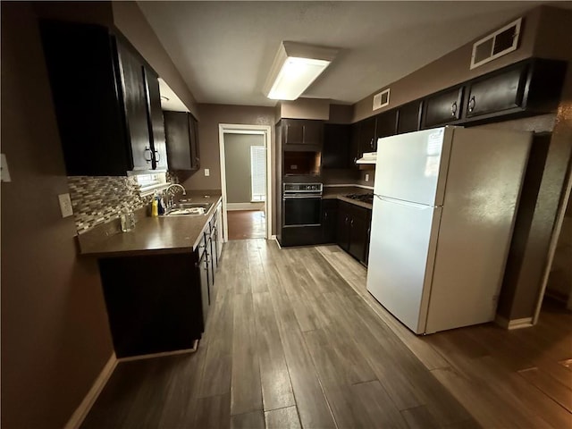 kitchen with sink, light wood-type flooring, oven, and white fridge