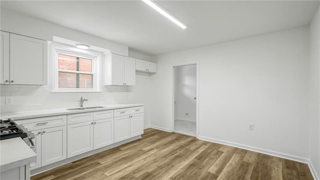 kitchen featuring sink, white cabinetry, light hardwood / wood-style flooring, stainless steel range with gas stovetop, and decorative backsplash