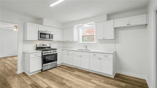 kitchen featuring appliances with stainless steel finishes, sink, white cabinets, backsplash, and light hardwood / wood-style flooring