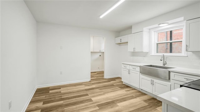 kitchen with white cabinetry, sink, backsplash, and light hardwood / wood-style floors