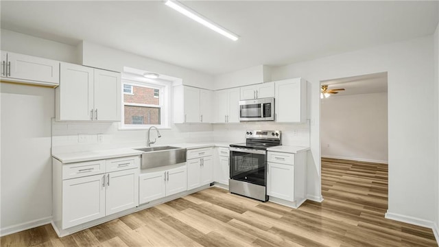 kitchen with sink, light wood-type flooring, ceiling fan, stainless steel appliances, and white cabinets