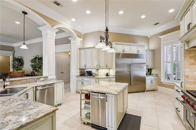 kitchen with ornate columns, appliances with stainless steel finishes, decorative light fixtures, sink, and light stone counters