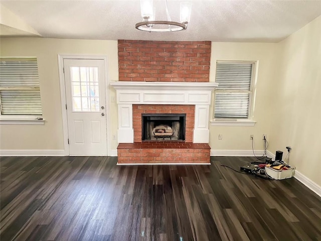 unfurnished living room with a brick fireplace, dark wood-type flooring, and a textured ceiling