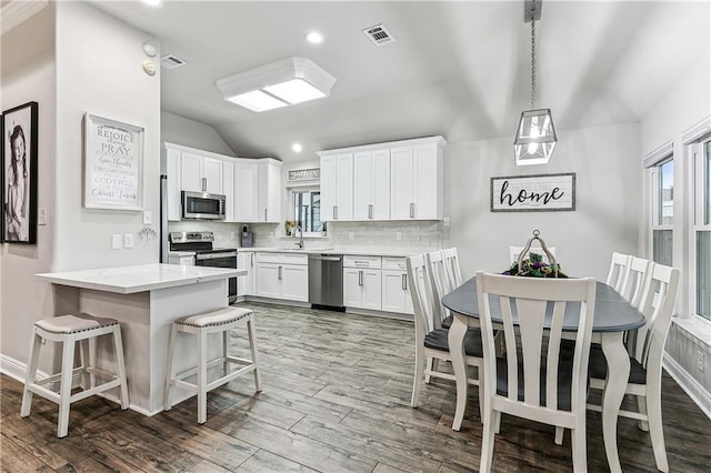 kitchen with lofted ceiling, a breakfast bar, white cabinets, and appliances with stainless steel finishes