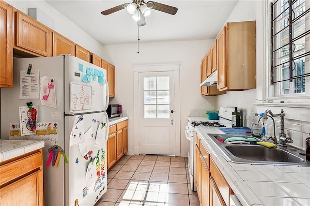 kitchen featuring tile countertops, sink, light tile patterned floors, ceiling fan, and white appliances