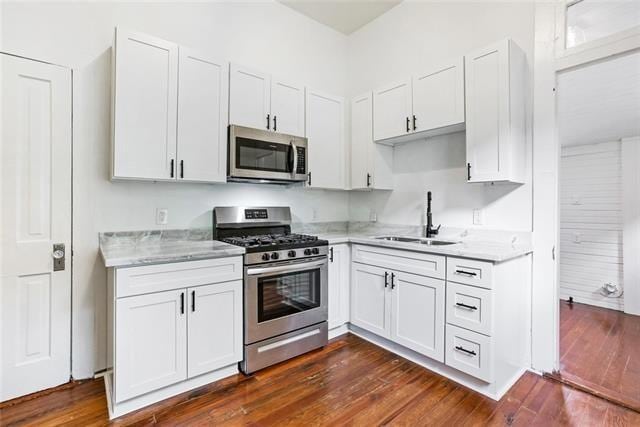 kitchen with sink, dark wood-type flooring, stainless steel appliances, light stone counters, and white cabinets