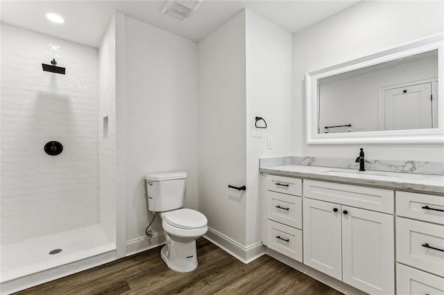 bathroom with hardwood / wood-style flooring, vanity, tiled shower, and toilet