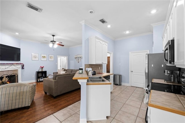 kitchen featuring sink, ornamental molding, tile counters, kitchen peninsula, and white cabinets