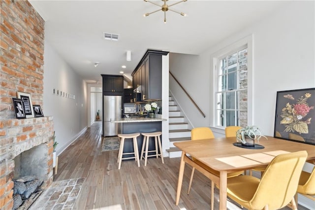 dining room featuring a brick fireplace, light hardwood / wood-style flooring, and a chandelier