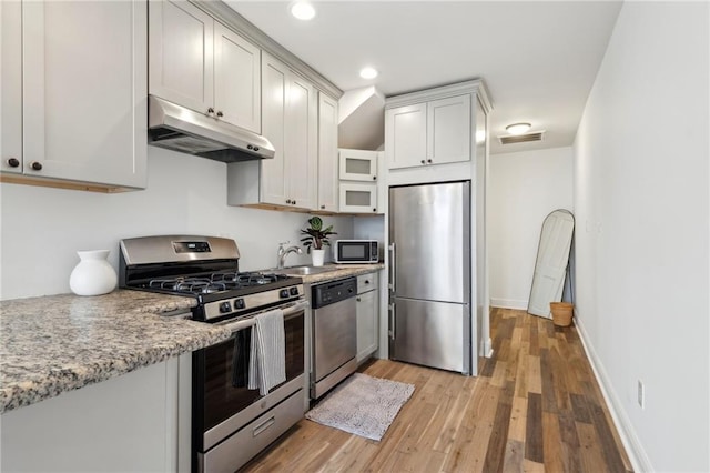 kitchen with sink, light hardwood / wood-style flooring, light stone countertops, and appliances with stainless steel finishes