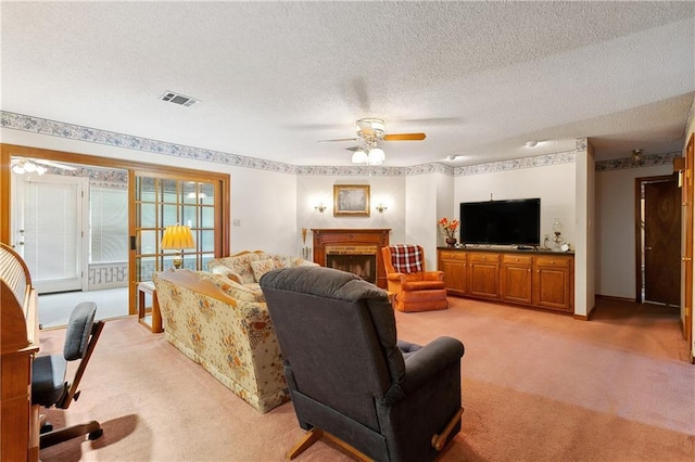 living room featuring light carpet, a fireplace, a textured ceiling, a ceiling fan, and visible vents