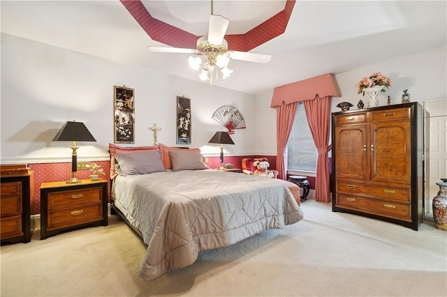 bedroom featuring light carpet, a ceiling fan, and a wainscoted wall