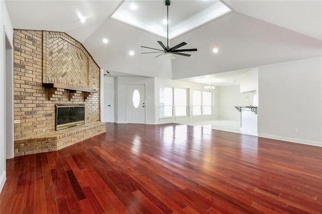 unfurnished living room featuring wood-type flooring, high vaulted ceiling, a brick fireplace, ornamental molding, and ceiling fan with notable chandelier