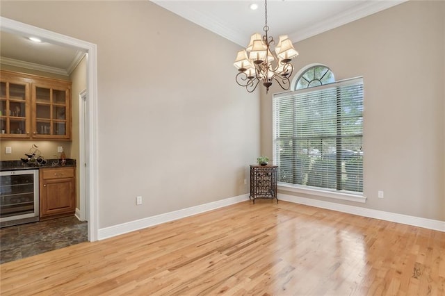 unfurnished dining area with bar, crown molding, a chandelier, beverage cooler, and light hardwood / wood-style floors